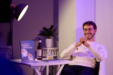 © Oliver Borchert Ein Autor sitzt neben einem Tisch mit seinem Buch
